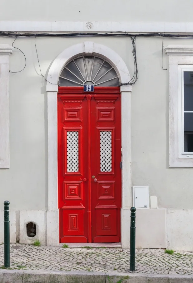 Una puerta de entrada roja con paneles y una ventana arqueada encima.