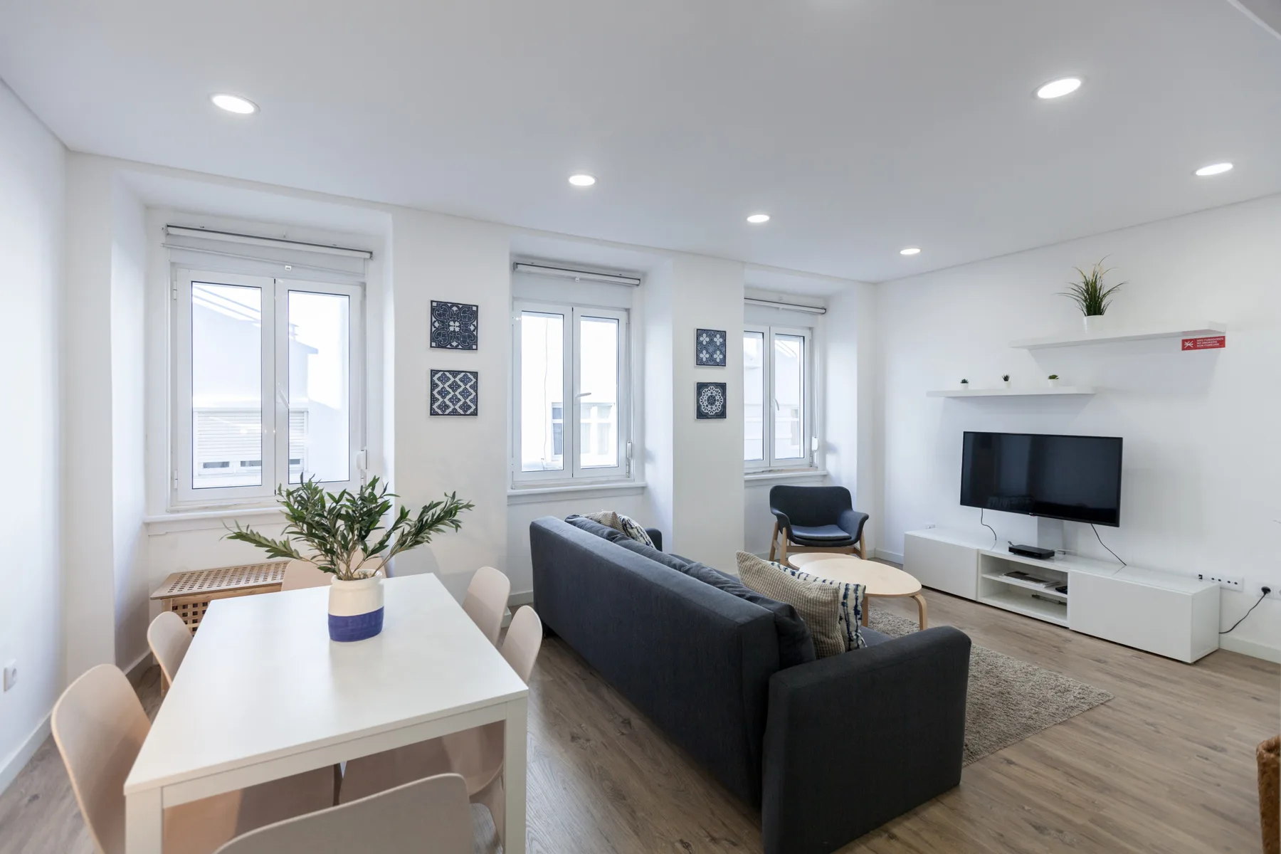 A bright living and dining area with seating, a television, and tall windows.