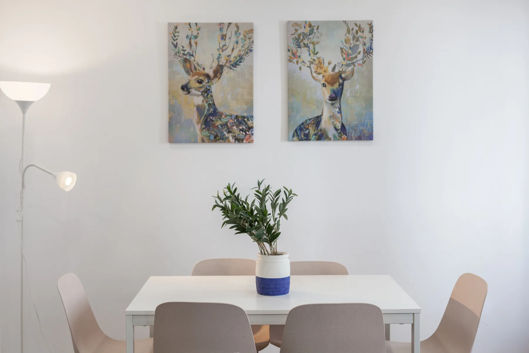 A dining area with a white table, seating, and two wall paintings.