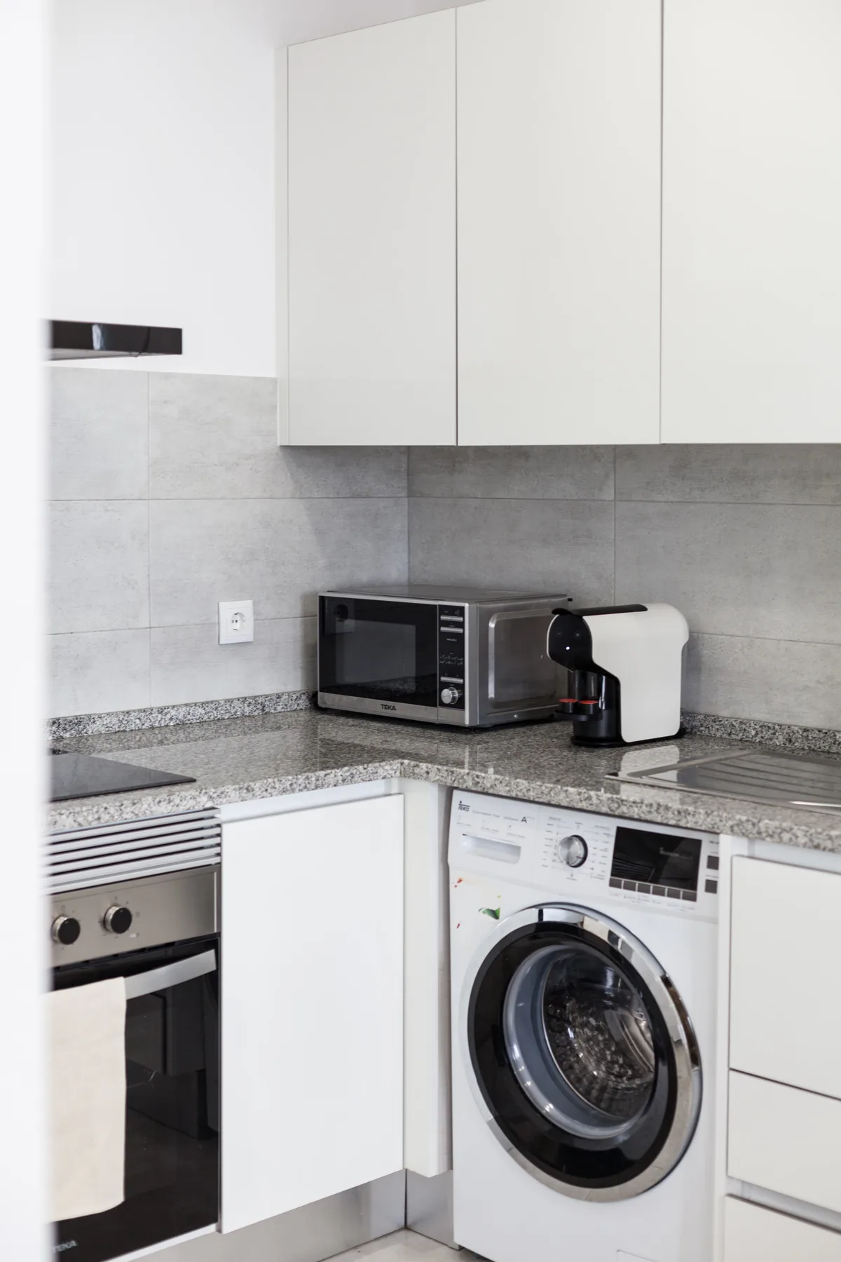 Una cocina compacta con armarios blancos, un microondas y una lavadora de carga frontal.