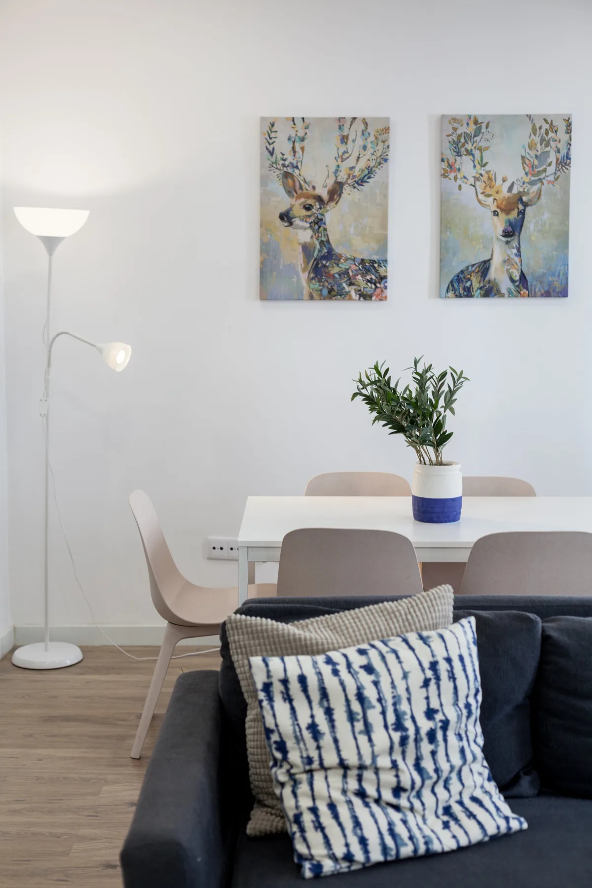 A living and dining area with a dark sofa, table, and colorful deer paintings.