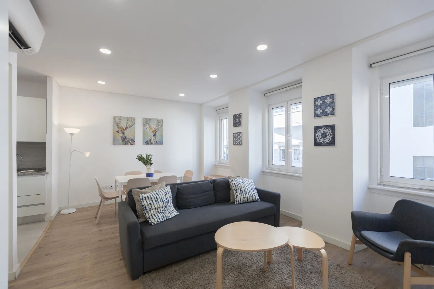 A bright living room with dark seating, light wood tables, and wall art.
