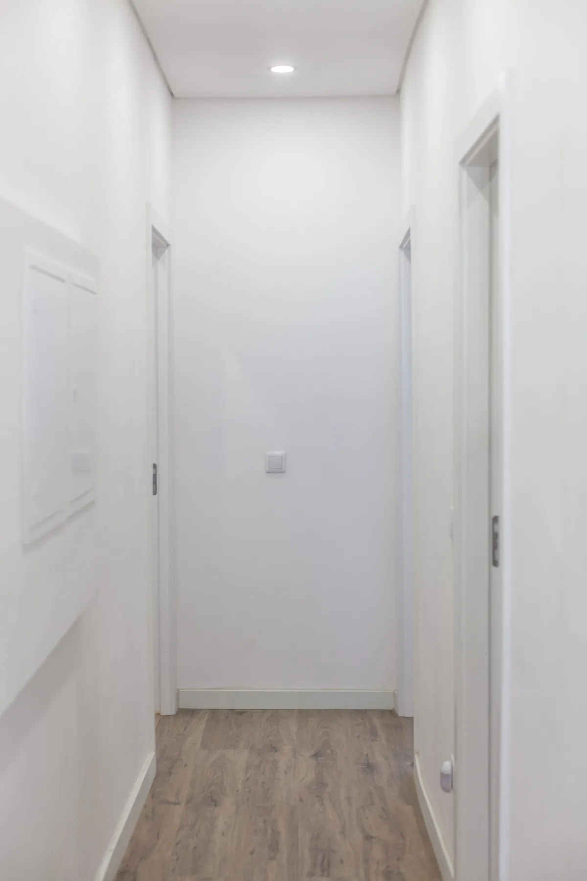 Un pasillo estrecho con paredes blancas, varias puertas y suelo efecto madera.