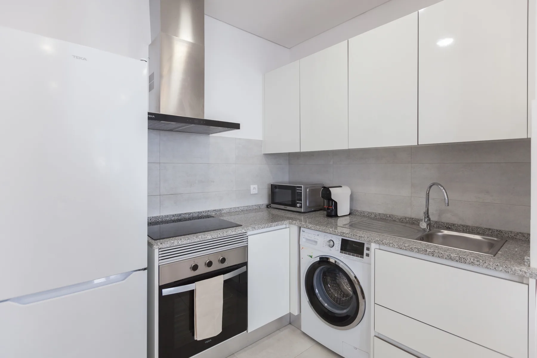 A compact kitchen with white cabinets, a countertop, and built-in appliances.