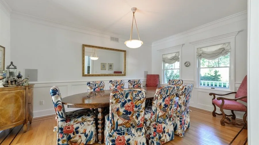 A dining room with a round table, patterned seating, and tall windows.