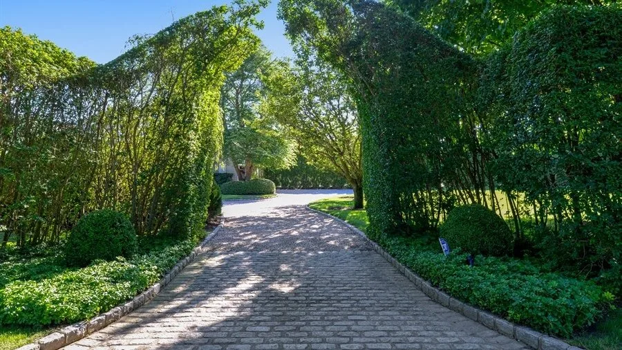 Un camino pavimentado de jardín se curva bajo un arco de setos frondosos.