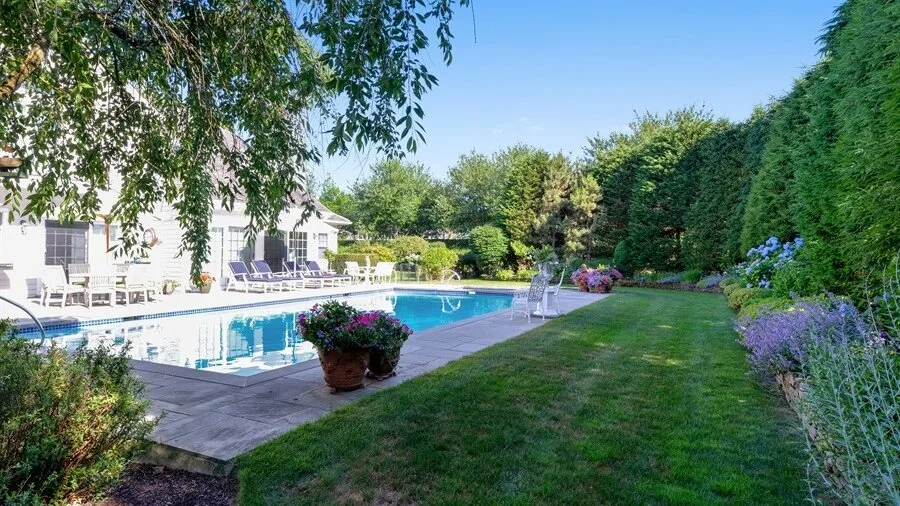 Un césped de jardín bordea una piscina junto a un edificio blanco y setos frondosos.