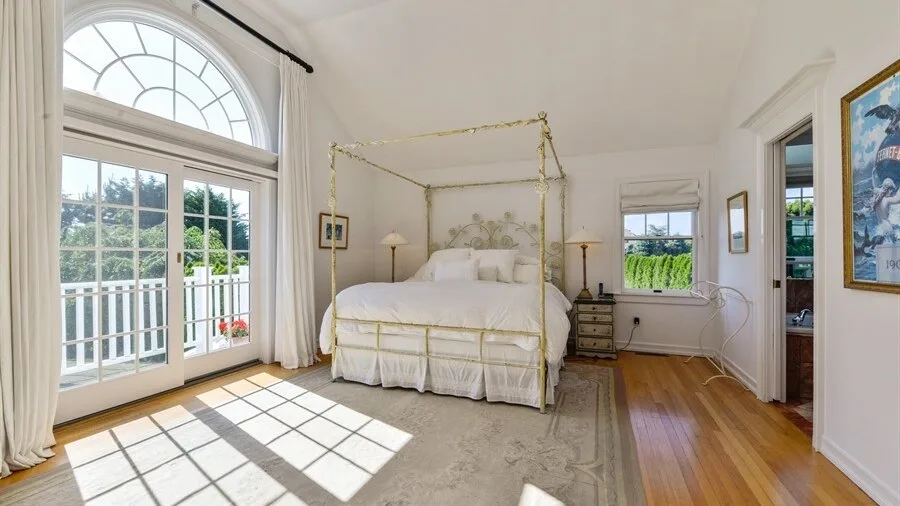 Un dormitorio luminoso con una cama con dosel y grandes ventanas arqueadas.