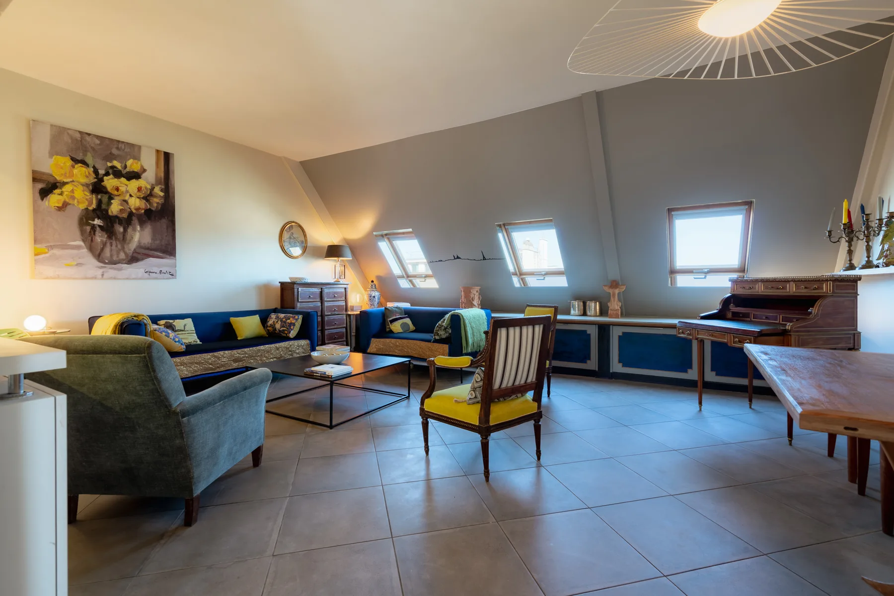 A furnished lounge with seating, a desk, and sloped ceilings beneath skylights.