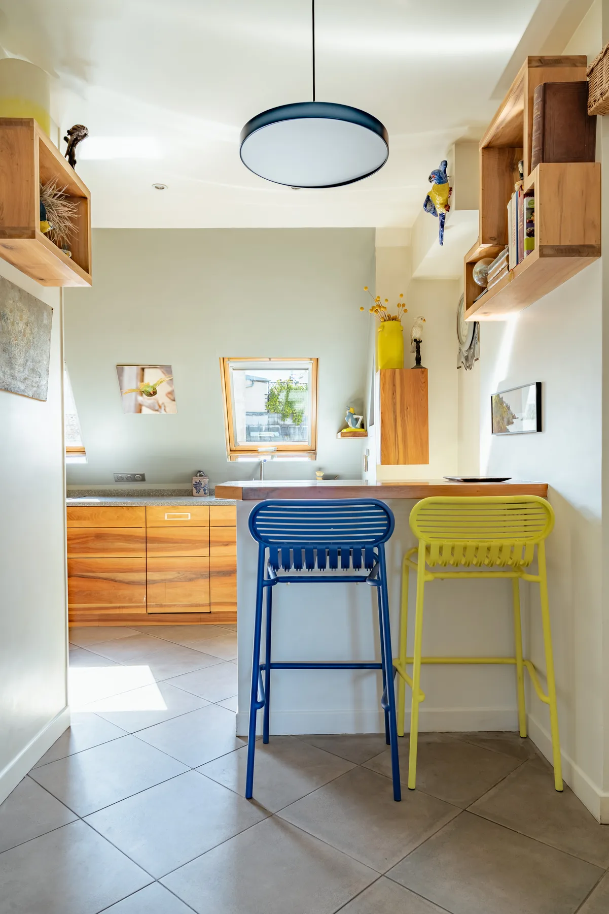 A bright kitchen with wooden cabinets and blue and yellow bar stools.