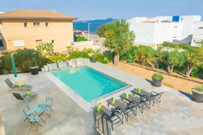 Una piscina al aire libre ocupa un patio pavimentado con asientos y vegetación alrededor.
