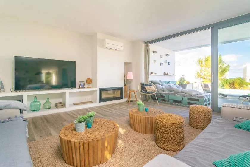 Una sala luminosa con televisor, asientos bajos y una gran abertura de vidrio hacia el patio.