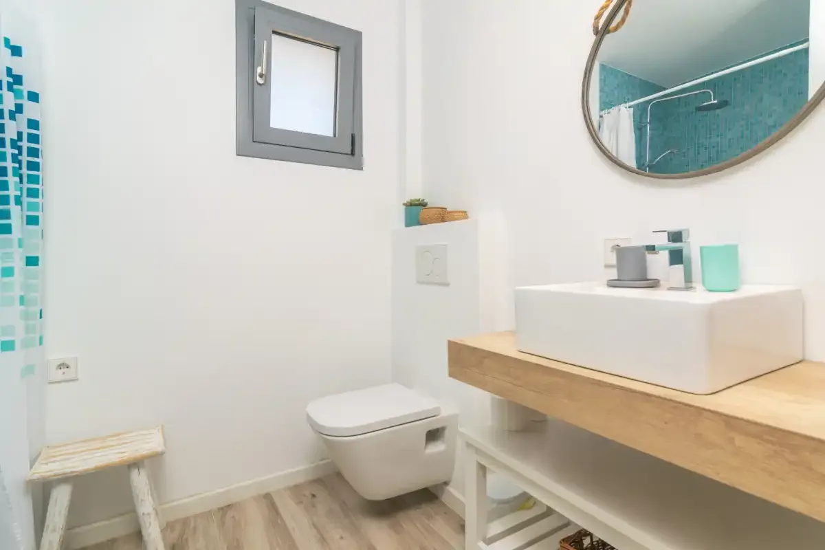 Un baño luminoso con un lavabo suspendido y detalles de azulejos turquesa.