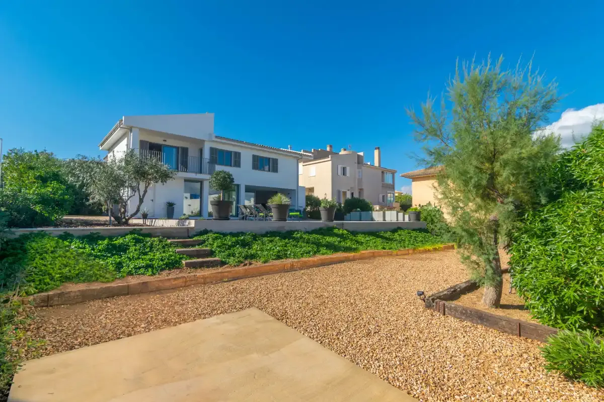 Una casa moderna se encuentra tras un jardín de grava con árboles y arbustos.