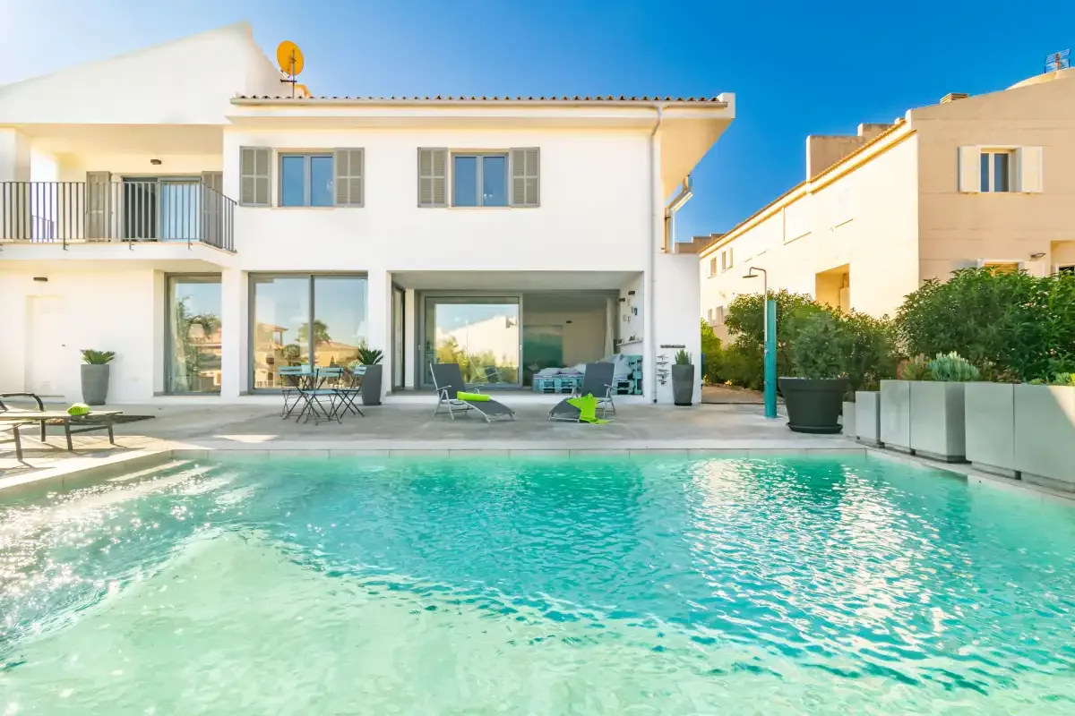 Una casa blanca moderna da a una piscina turquesa y un patio.