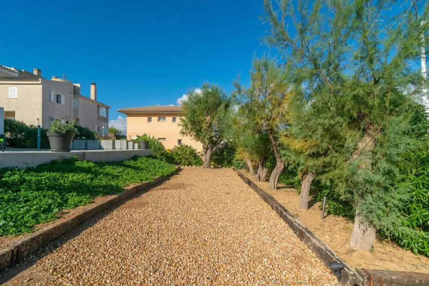 Un camino de grava pasa entre vegetación verde y árboles junto a edificios cercanos.