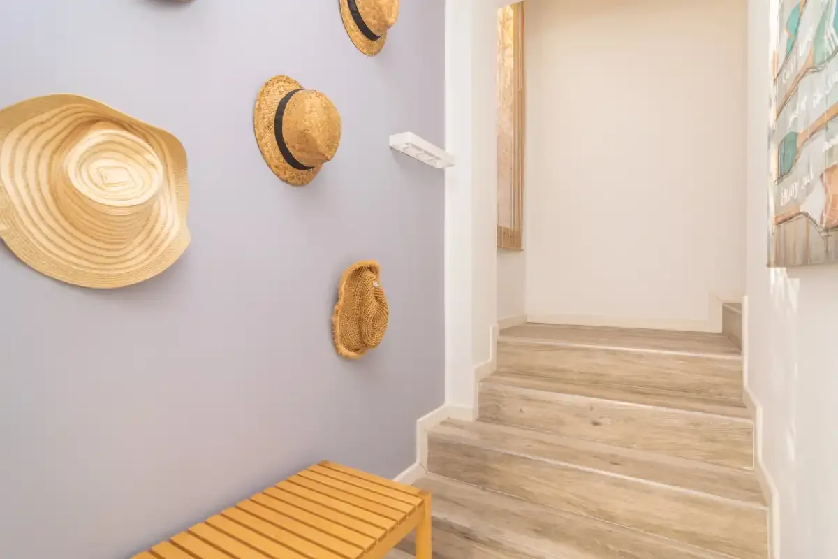 Un pasillo luminoso con escalones de madera y sombreros de paja en la pared.