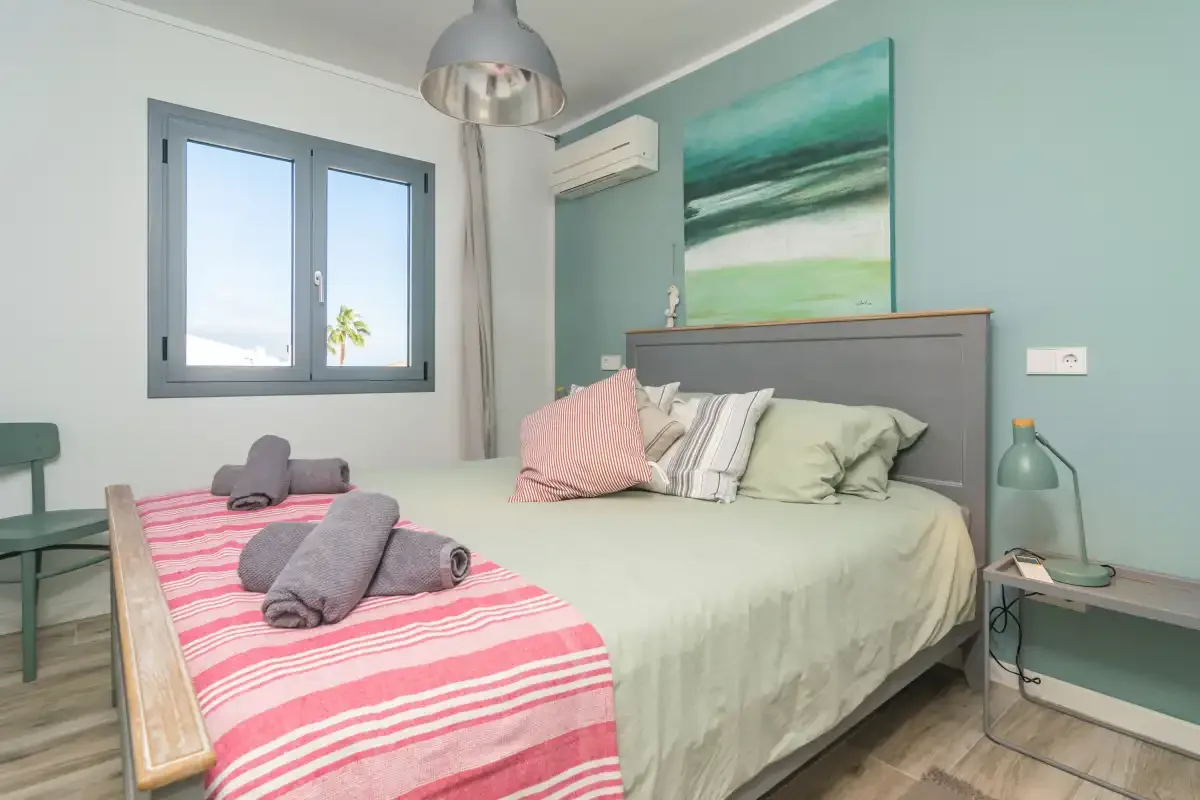 Un dormitorio con una cama bajo un cuadro marino y una ventana.