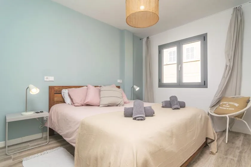 Un dormitorio con una cama vestida con ropa de cama clara y una ventana al lado.