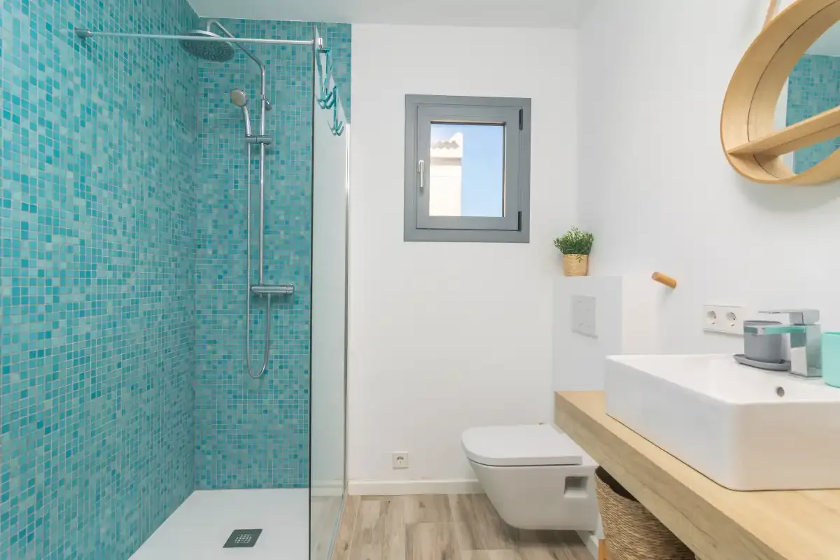 Un baño luminoso con ducha alicatada, inodoro y lavabo.