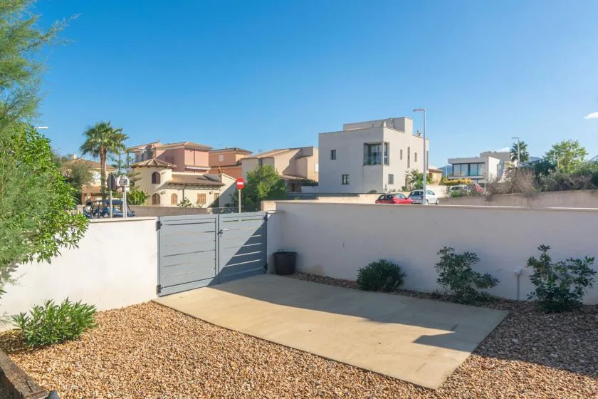 Una zona exterior pavimentada está delimitada por un muro bajo y una puerta metálica.