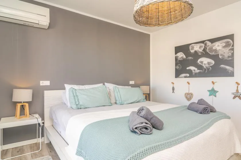 Un dormitorio con una cama bien tendida, ropa de cama verde agua y arte en la pared.