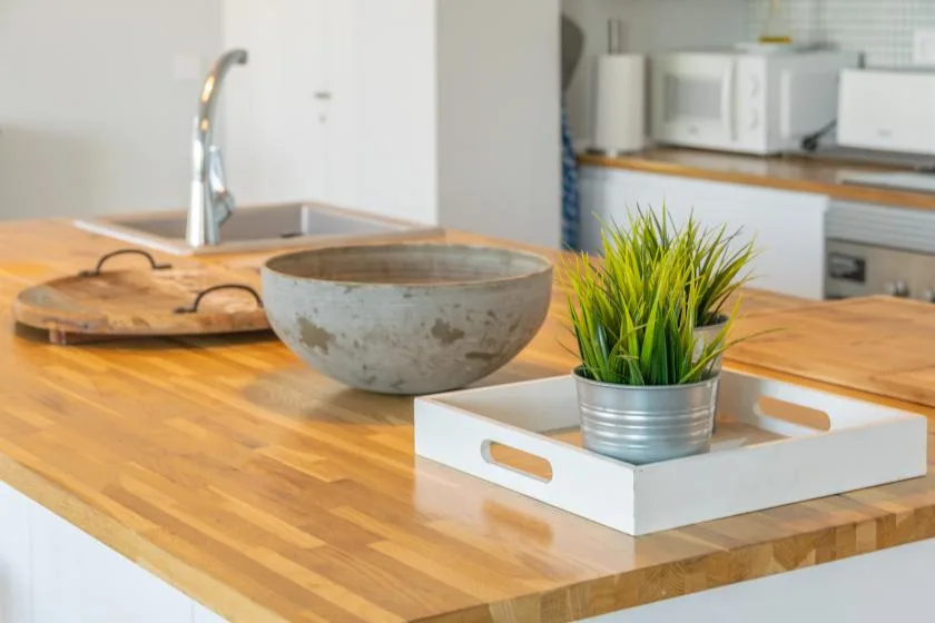 Una encimera de cocina con superficie de madera, un cuenco y una planta en maceta.