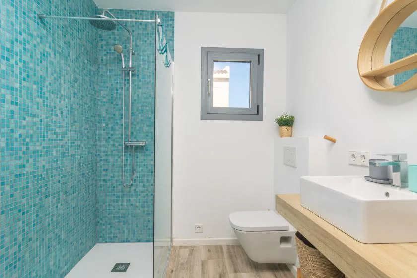 Un baño con ducha de azulejos turquesa, inodoro y lavabo.