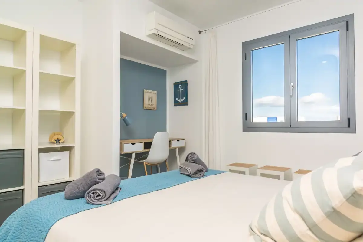 Un dormitorio luminoso con una cama, estanterías empotradas y una ventana con vistas al cielo.