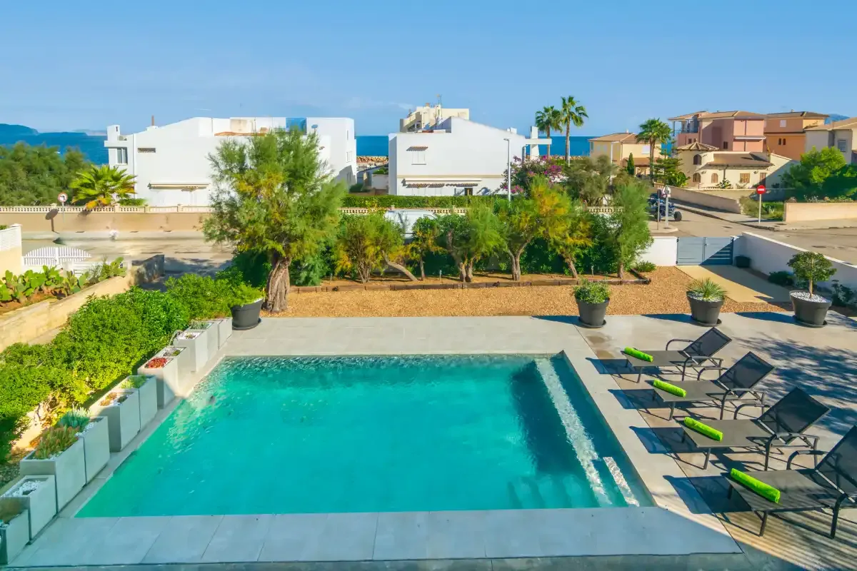 Una piscina al aire libre rodeada de asientos reclinables y vegetación.