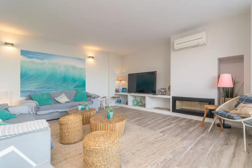 Luminoso salón con asientos, un televisor y un gran mural de olas del mar.
