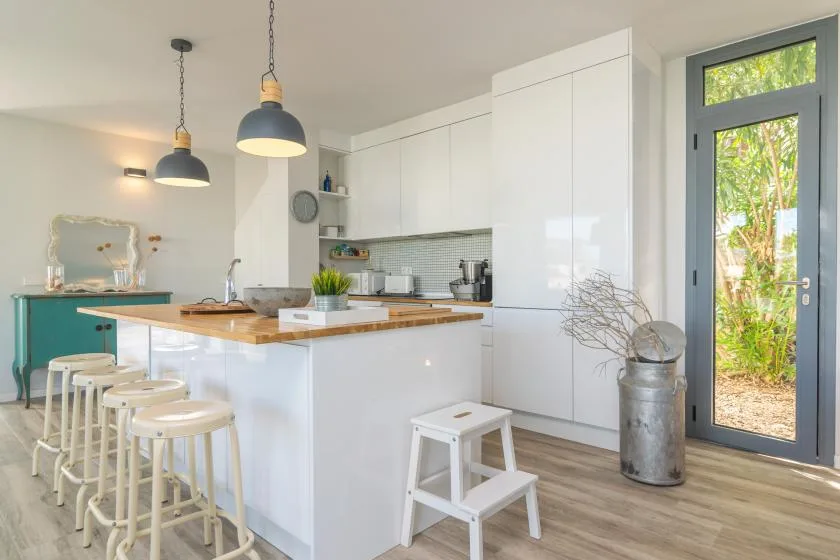 Una cocina luminosa con una isla blanca, encimera de madera y lámparas colgantes.