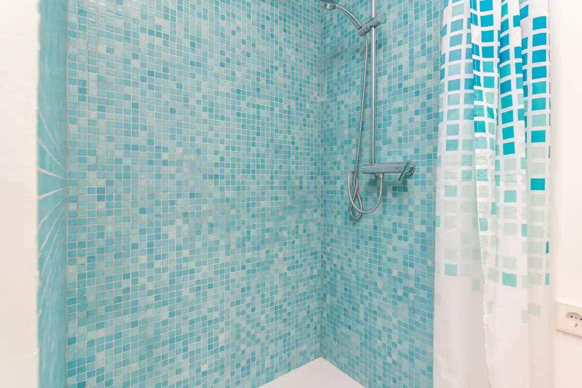 Una ducha con paredes de mosaico turquesa y una cortina estampada.