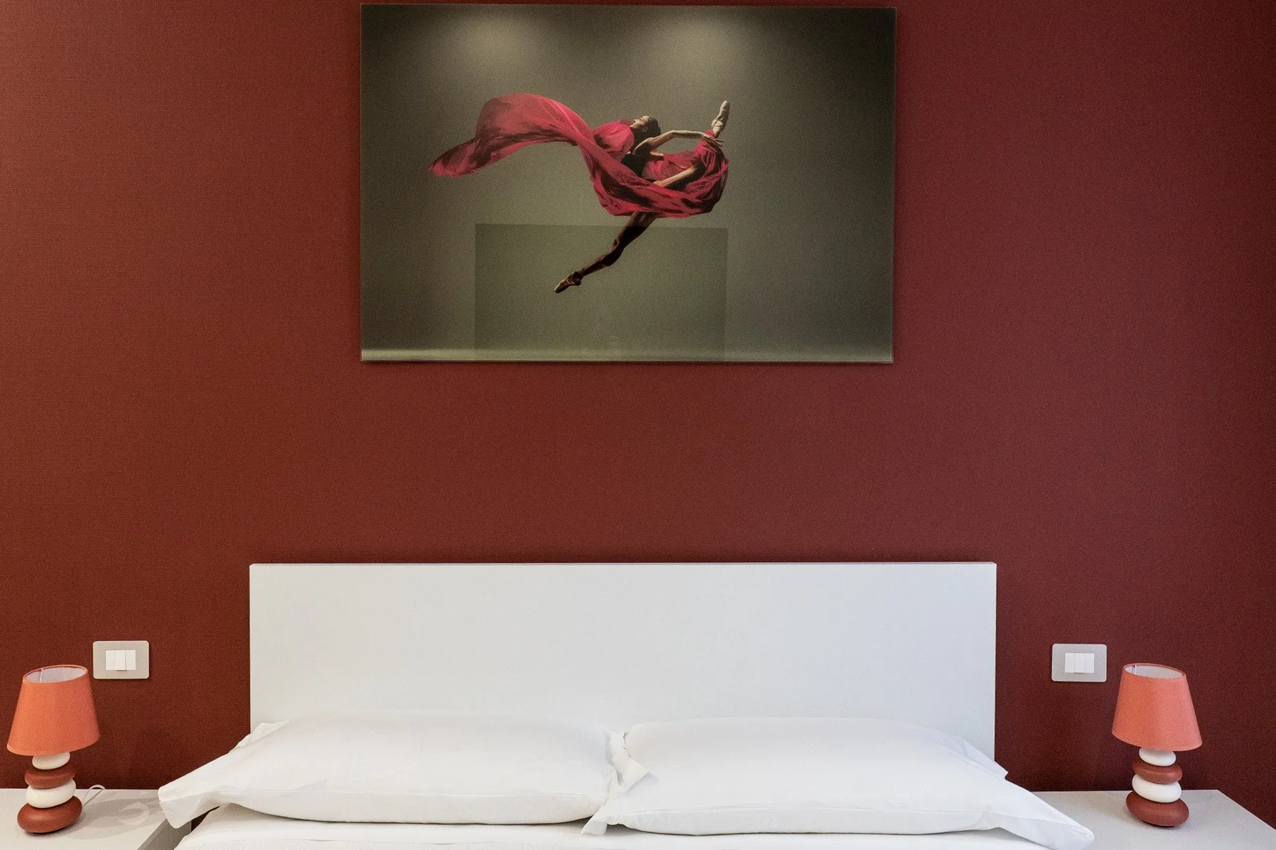 A bedroom with a bed beneath framed artwork on a red wall.