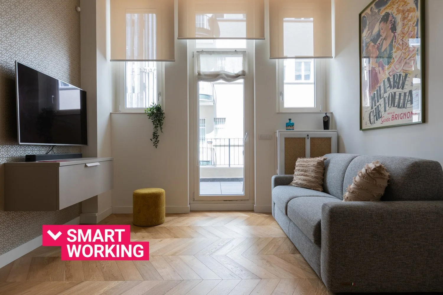 Una sala luminosa con sofá, televisor y puertas de cristal que dan a un balcón.