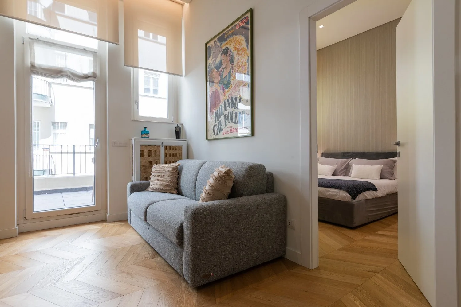 Una luminosa sala de estar con un sofá gris junto a la entrada de un dormitorio.