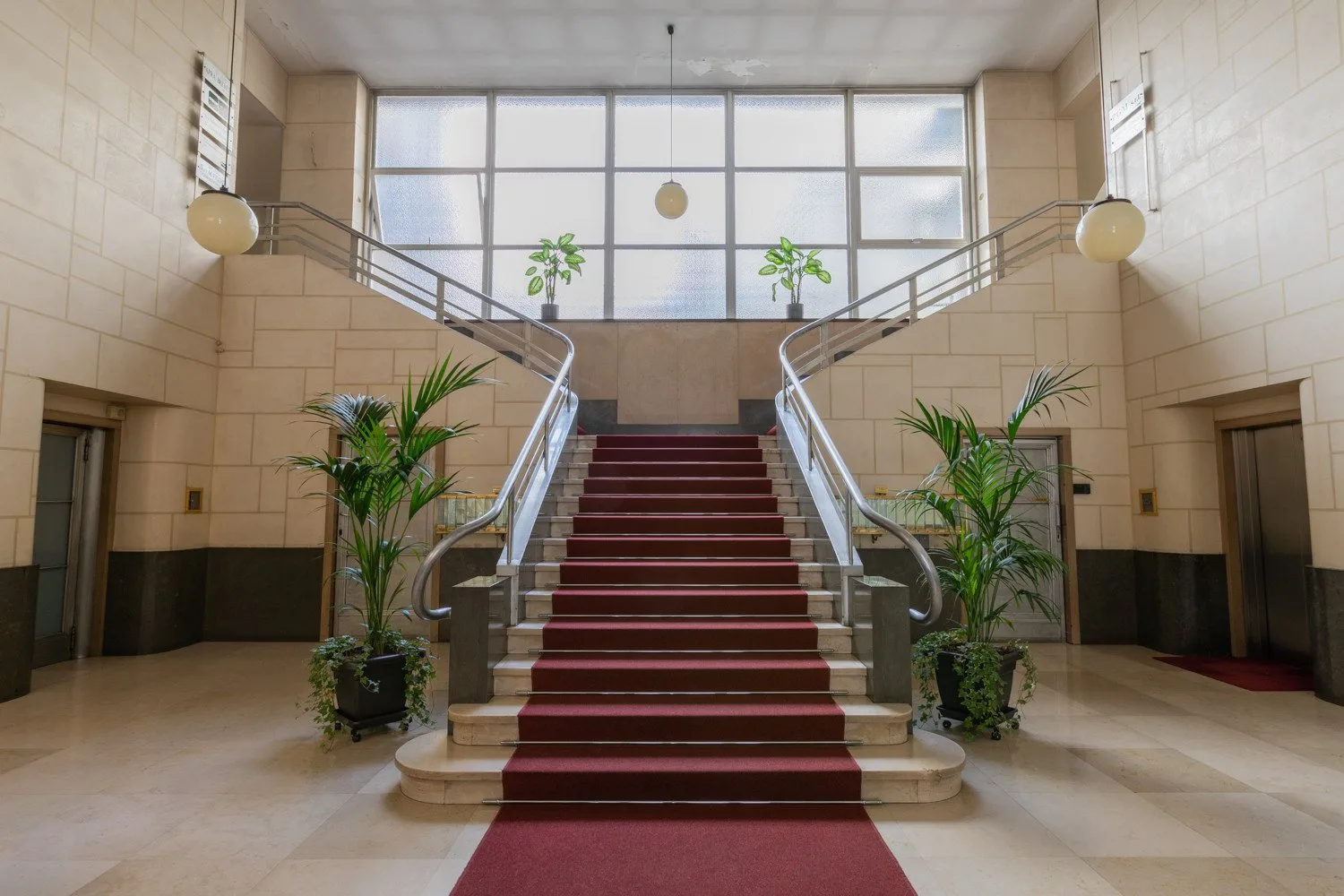Un amplio vestíbulo presenta una escalera central con alfombra roja y grandes ventanas.