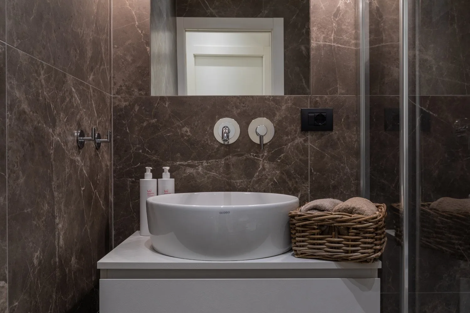 Un lavabo de baño con cuenco redondo, espejo de pared y cesta tejida.