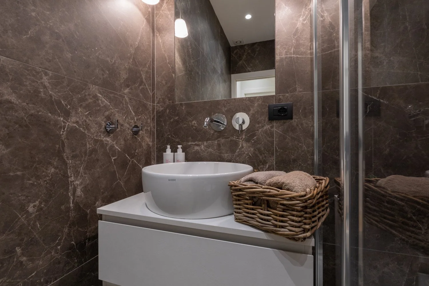 Un lavabo de baño con un lavamanos blanco, espejo y cesta tejida.