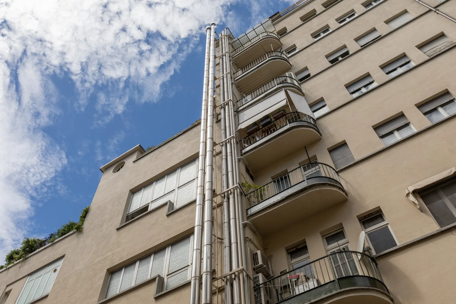 Vista exterior de un edificio de varias plantas con balcones bajo un cielo parcialmente nublado.