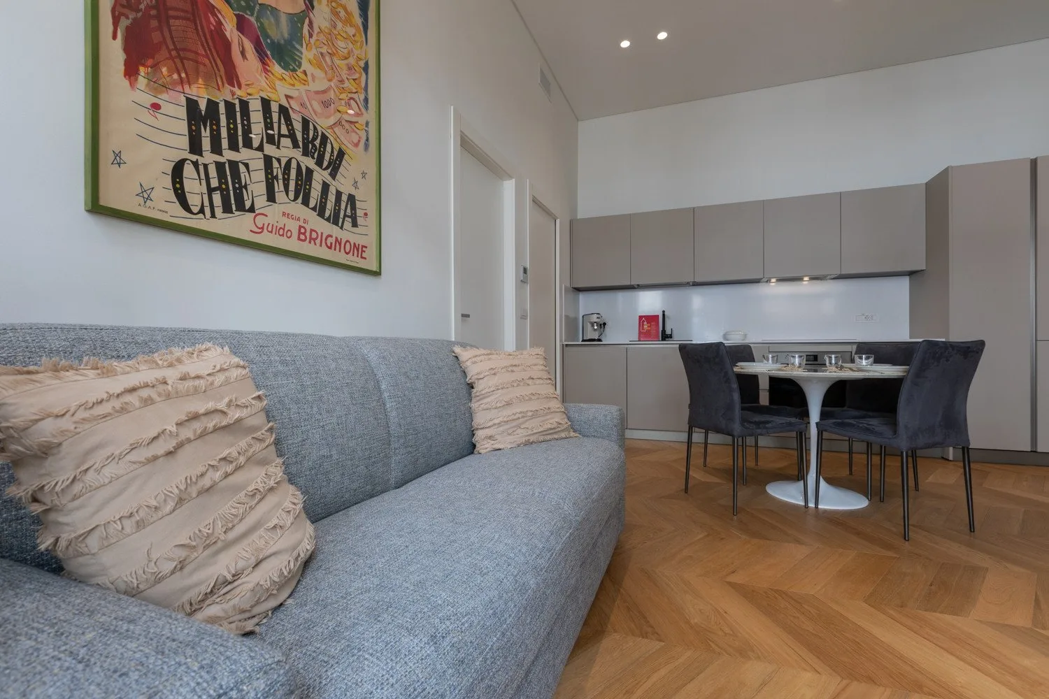 Una zona de estar y comedor con un sofá gris y una mesa junto a la cocina.