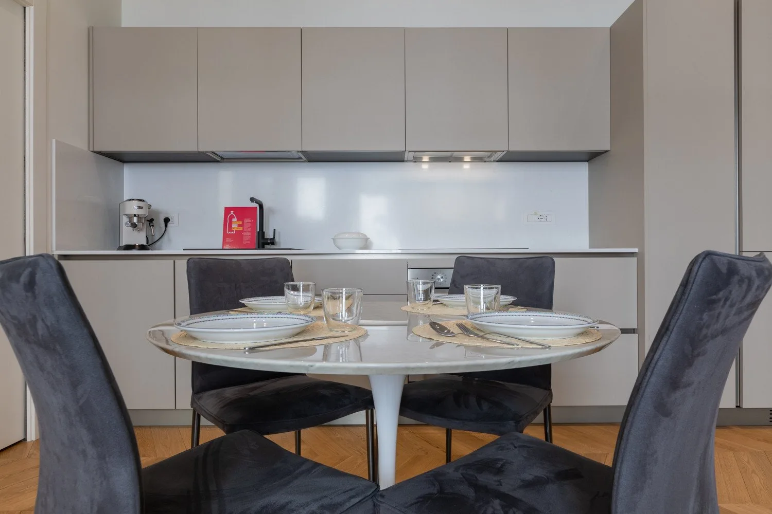 Una mesa de comedor con cubiertos está frente a una cocina compacta.