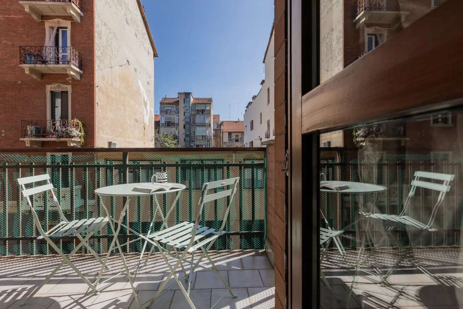 Un pequeño balcón con asientos al aire libre da a edificios de apartamentos vecinos.