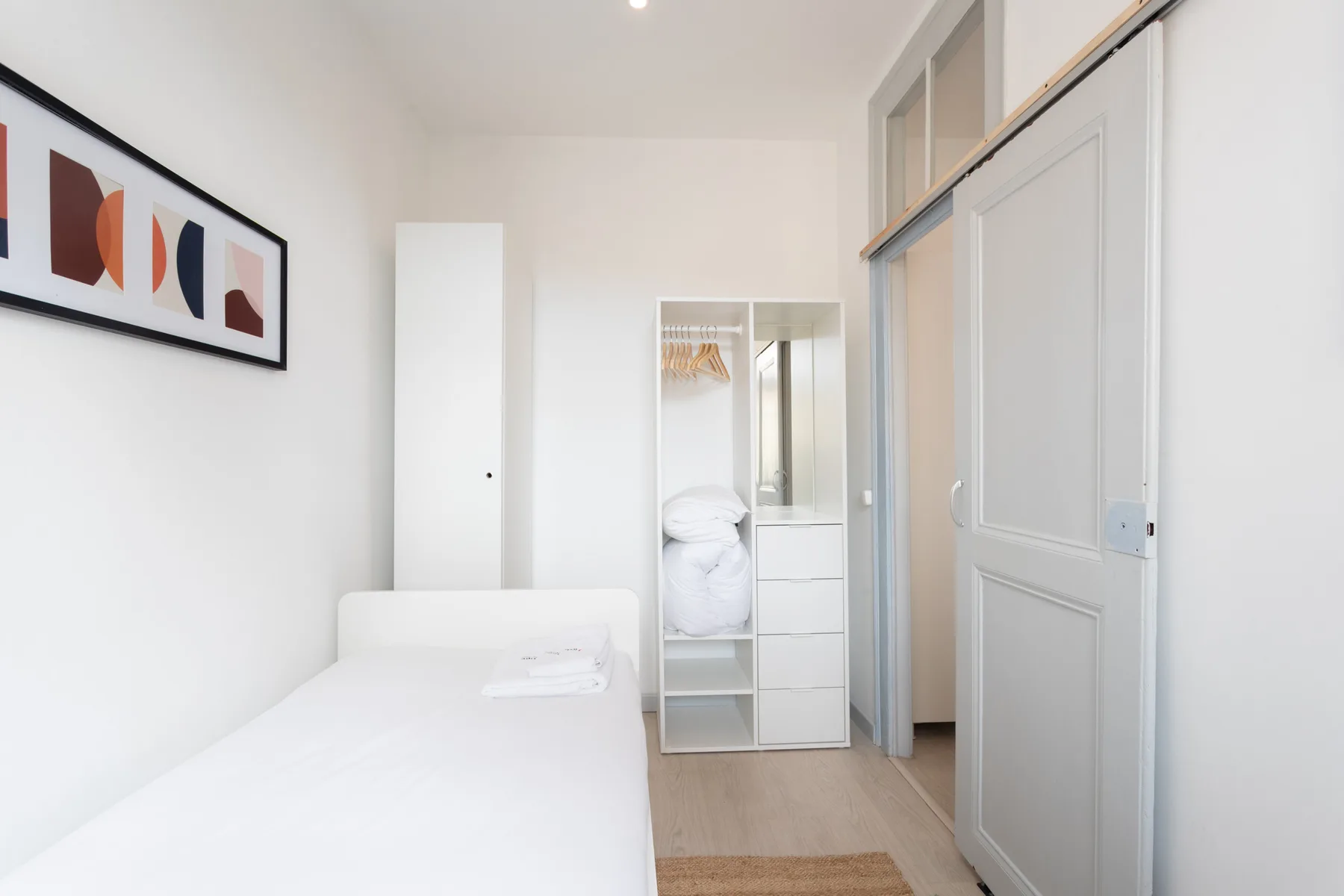 A bright bedroom with a bed, framed abstract art, and a mirrored wardrobe.