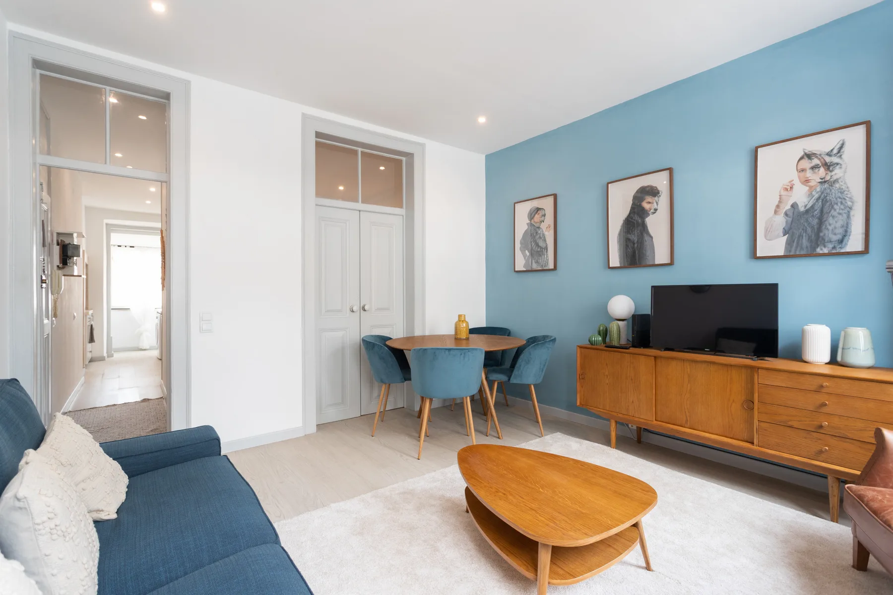 A bright living room with blue seating, a wooden coffee table, and framed artwork.