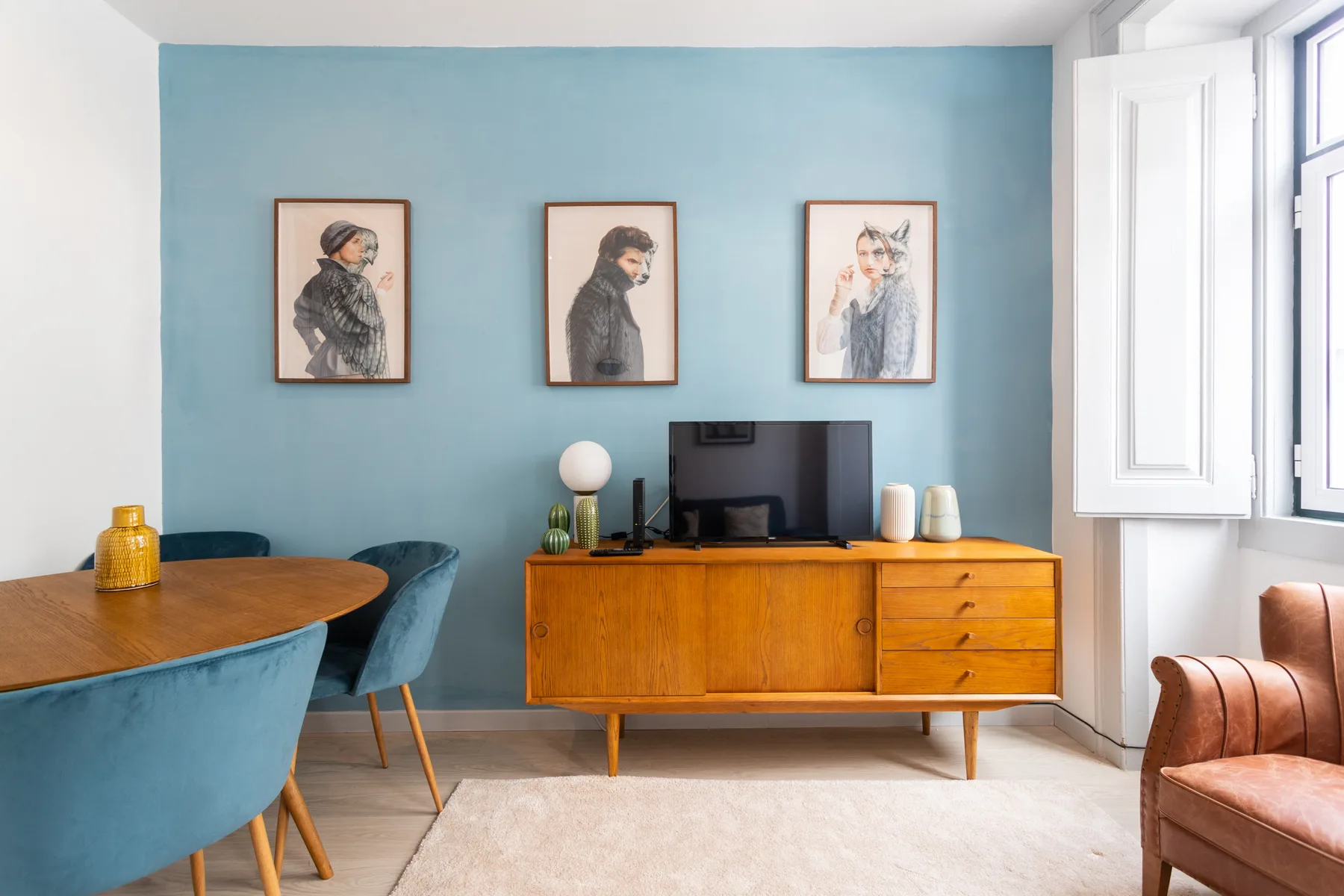 A living room with a wooden media cabinet beneath three framed portraits.