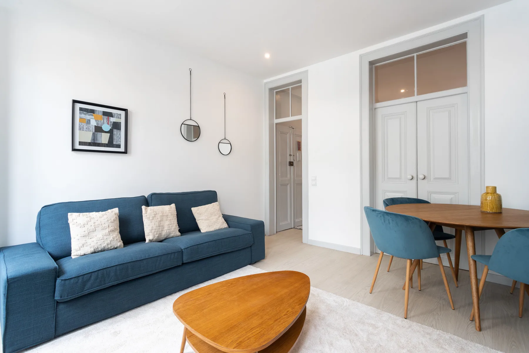 A bright living room with blue seating, a wooden coffee table, and a dining area.