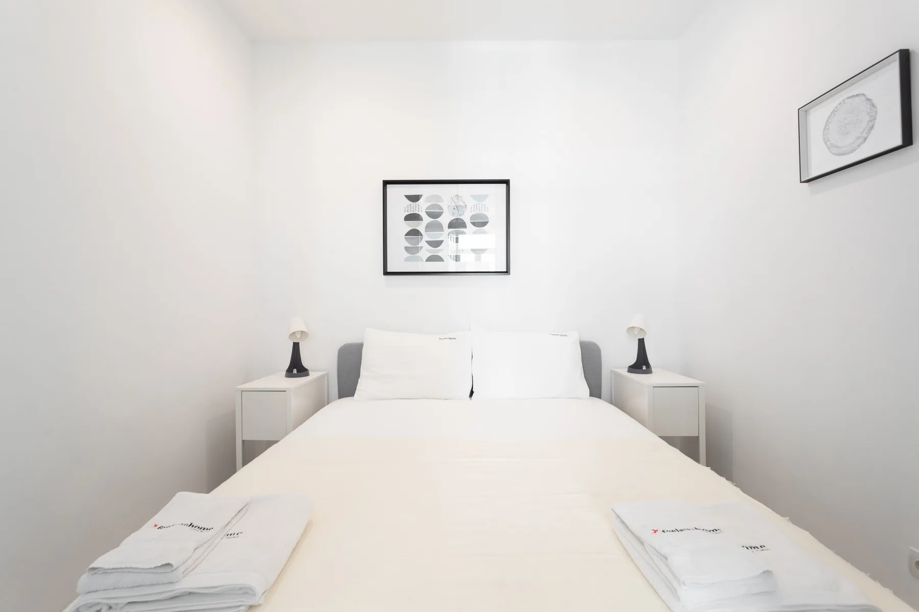 A bright bedroom with a neatly made bed and framed artwork.