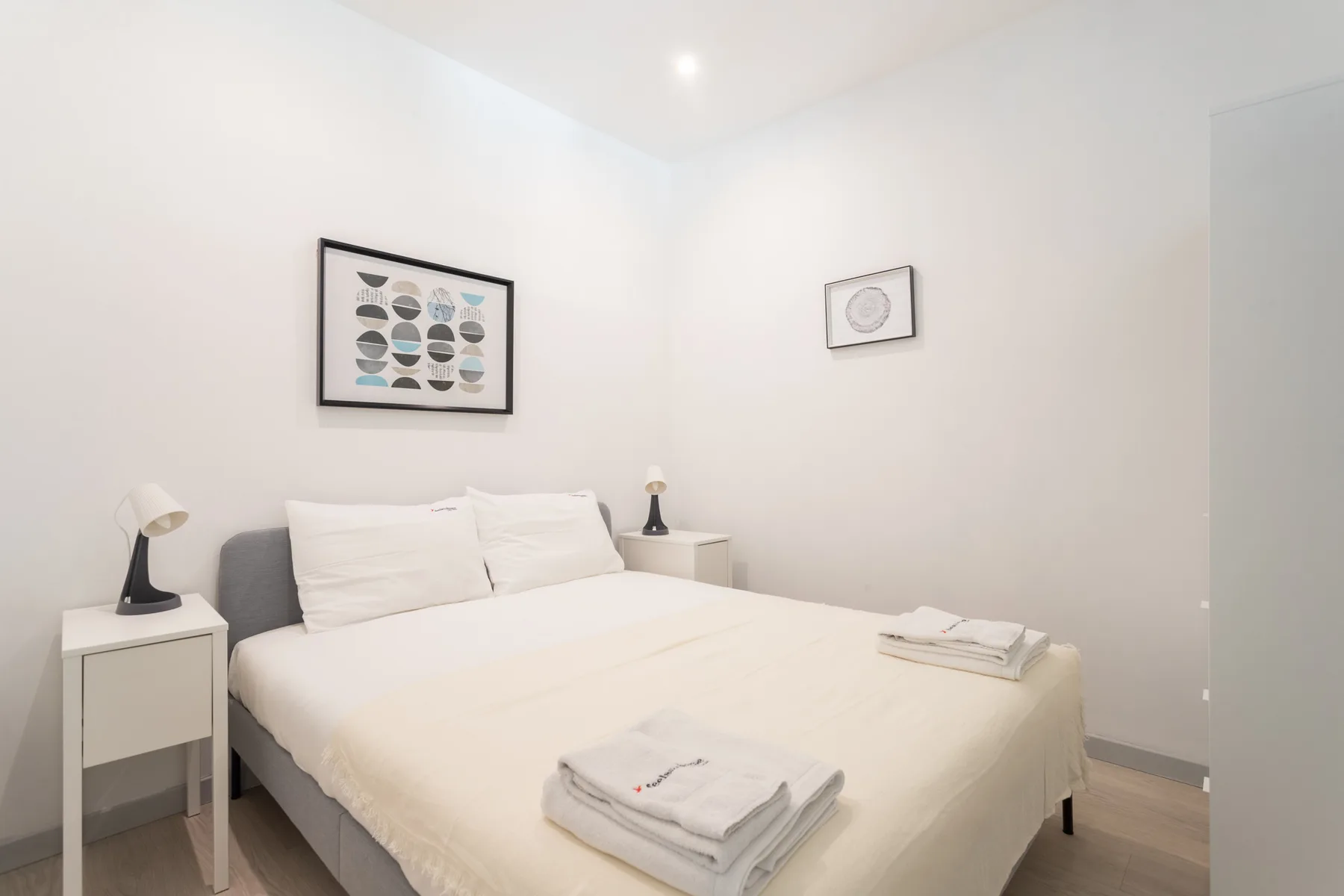 A bright bedroom with a neatly made bed and framed wall art.