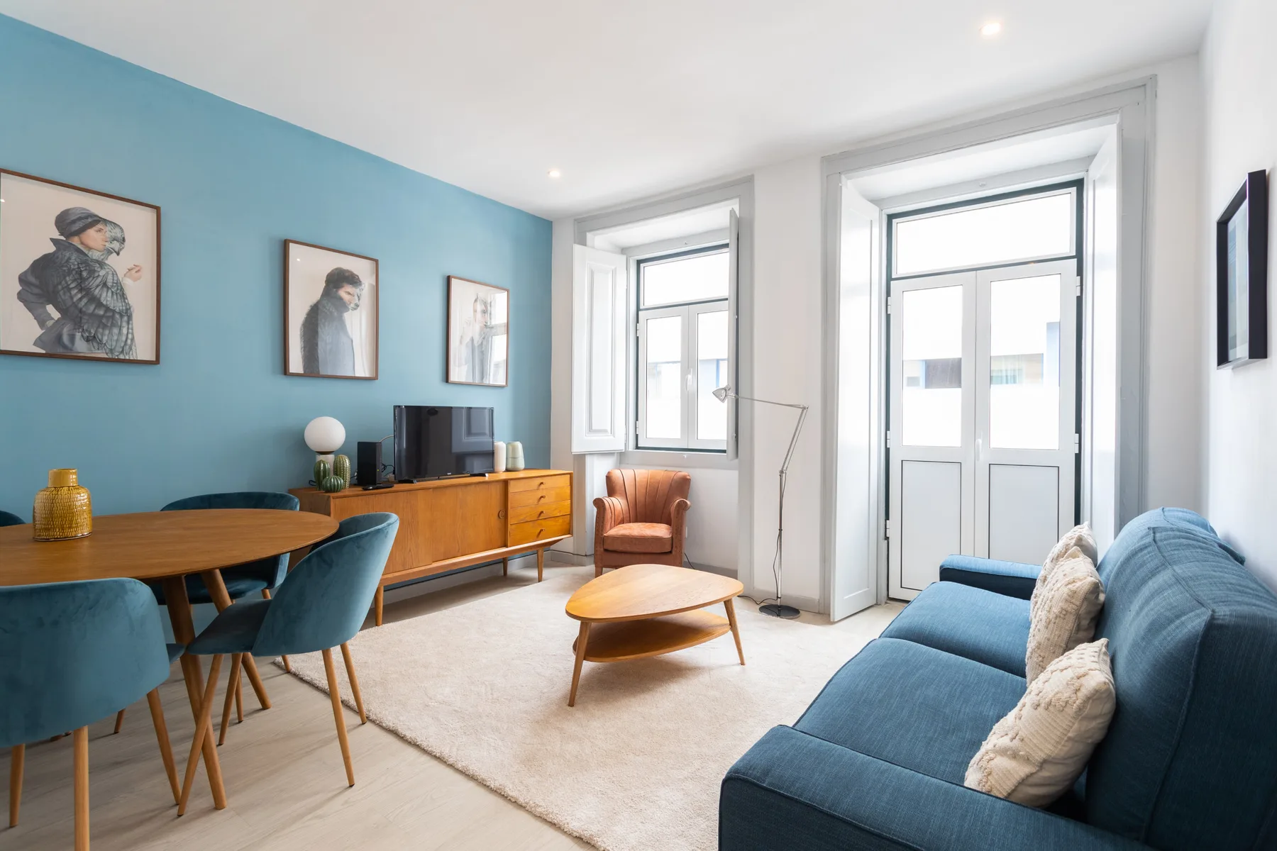 A bright living room with blue seating, a dining table, and tall windows.